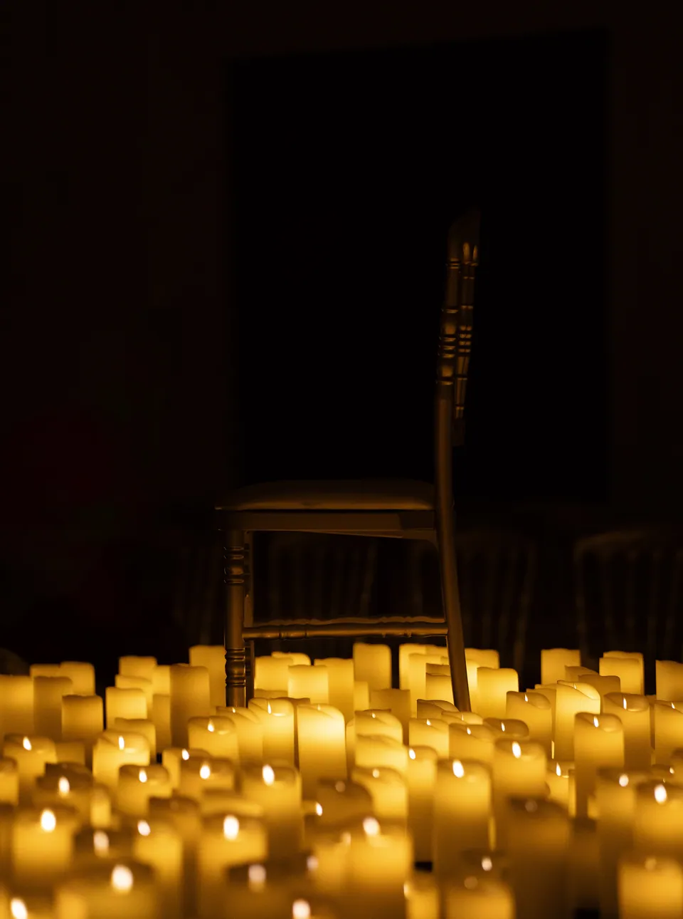 A single chair standing amid a floor of lit candles