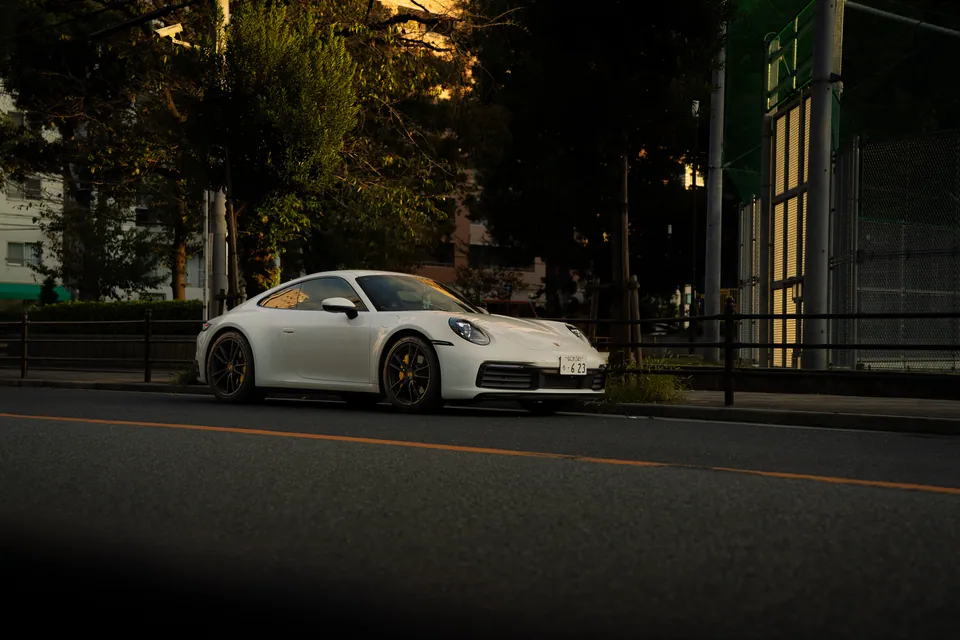 White sports car on a tree-lined road at dusk
